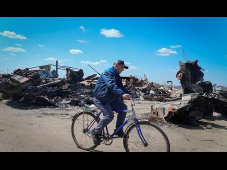 A local resident rides a bike past a destroyed Russian military vehicle in Bucha, on the outskirts of Kyiv, Ukraine, Tuesday, May 10, 2022.