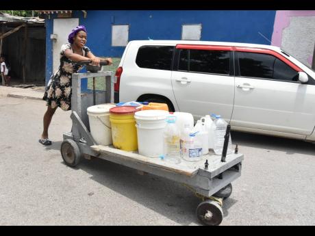 Nadia Williams pushes a handcart with buckets to catch water at a makeshift well in Majesty Gardens on Wednesday. 
