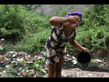 Nadia Williams washes her face with water sourced from a makeshift well located in Majesty Gardens, St Andrew, on Wednesday. Residents say the community has been without running water for weeks. 