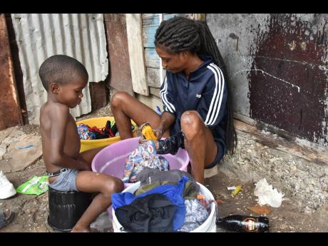 Jody Reid and her son, Dwayne Richards, wash clothes outdoor in the community of Majesty Gardens, St Andrew, on Wednesday. The community has been without piped water for weeks.