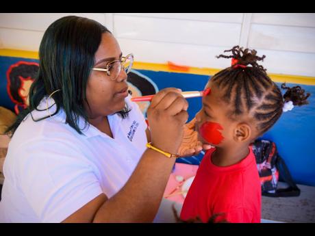 Caribbean Flavours and Frangrances Quality Assurance Manager Joddian Howard decorates the face of Katahlie Ormsby of End Time Basic School, St Andrew.