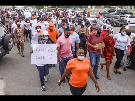 Followed by protesters, Mark Golding (in blue Kangol cap), leader of the Opposition, marches with a copy of a draft ministerial order to the Ministry of Finance and the Public Service Monday. 