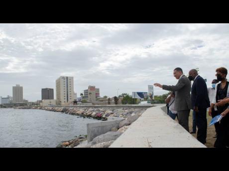 Prime Minister Andrew Holness waves to a fisherman out at sea  at the official handover ceremony for the Port Royal Revetment project adjacent to the Breezy Castle sports complex on Wednesday. Looking on are Dr Wayne Henry, chairman of the Jamaica Social I