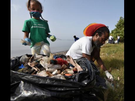 Habte Selassie Brown and his daughter Aya help clear plastic bottles and other debris from Sirgany Beach in east Kingston during a clean-up drive on Saturday. Aya, who is six years old, is a member of an environmental club at Liberty Learning Centre in Tow