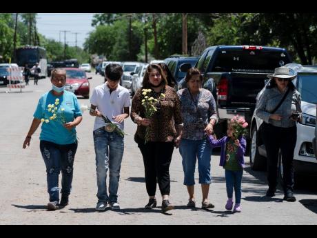People walk with flowers to honour the victims in Tuesday’s shooting at Robb Elementary School in Uvalde, Texas, on Wednesday. Desperation turned to heart-wrenching sorrow for families of grade schoolers killed after an 18-year-old gunman barricaded hims