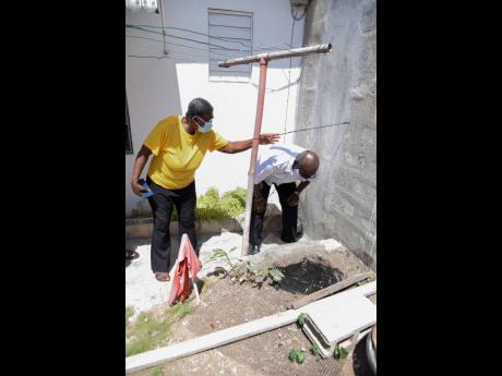 Ethel Oeat-Smith (left), a resident of Harbour Drive in St Andrew, shows Local Government Minister Desmond McKenzie how the water flowing beyond her wall is eroding the land under her home during a tour yesterday.