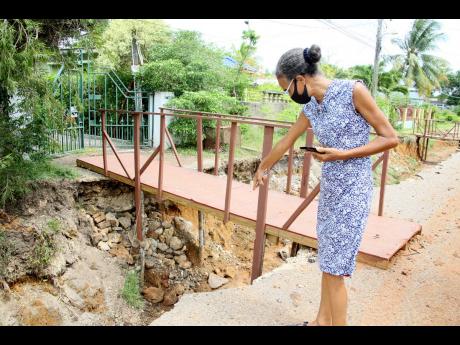 Lorelei Mulgrave of Treadlight Street in Clarendon points to an area where she attempted to place stones after erosion undermined the foot bridge used to access her home. Work started in December 2020 and has paused several times.