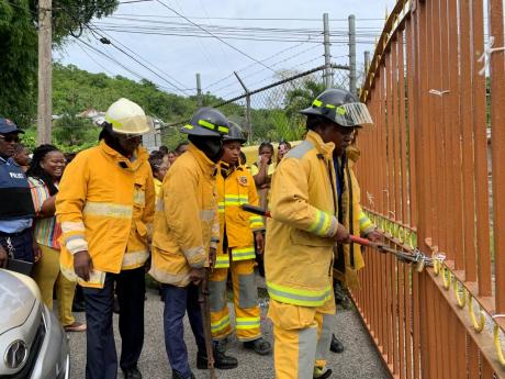 Firefighters removing a padlock from the front gate of Anchovy High School in St James on Monday. Auxiliary staff had locked the gate in protest for the removal the school’s bursar.