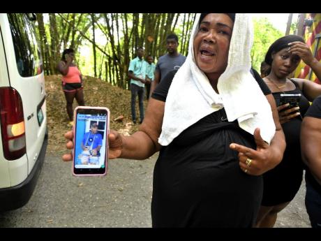 Lorna Lindsay, daughter of Derrick Lindsay, shows photo of her father after burnt remains believed to be those of the 77-year-old were found in Cavaliers, St Andrew, on Monday, two days after he went missing. A nephew is being sought by the police for ques