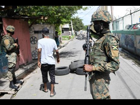 A resident walks past soldiers on a road in Spanish Town, St Catherine, on Wednesday. Fearful of reprisals after three men were killed a day earlier, residents littered the road with tyres to slow down potential attackers. 