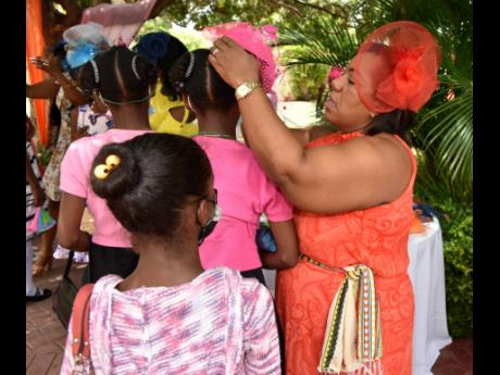 Chief Executive Officer of the Child Protection and Family Services Agency (CPFSA), Rosalee Gage-Grey, affixes a fascinator on a ward of the state during the CPFSA girls’ empowerment tea party help at Tropical Elegance on Saturday, June 18.