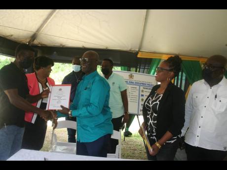 Rural Development Minister Desmond McKenzie (centre) hands a copy of a signed contract to a representative from THLC Company Ltd (left), which has been contracted to do refurbishing at the Chambers Pen All-Age School in Hanover. Also looking on are Dr Mich