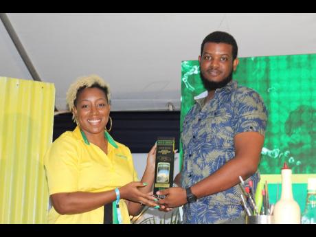 J. Wray & Nephew White Overproof Brand Manager Sasha Warner hands over a limited-edition Jamaica 60 bottle to Sean Mark Campbell after he answered a trivia question on the brand.