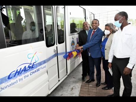 From left: Professor Dale Webber, principal of UWI, Mona, and W. Billy Heaven (second left), CEO of the CHASE Fund, cutting the ribbon during a handover of a 29-seater Coaster bus to the Faculty of Medical Sciences yesterday as Professor Minerva Thame, dea
