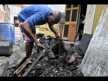 Trevor Watson goes through the charred rubble yesterday as he and other relatives began clean-up activities, a day after a fire destroyed their home at 20 Clarence Road in Craig Town in Kingston 12 on Thursday.