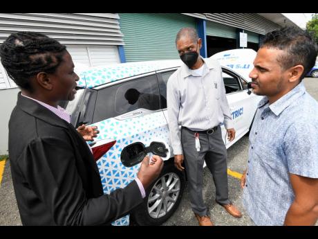 Richard Gordon (centre), manager of business development projects at the Jamaica Public Service Company (JPS) and project manager of the JPS EV-charging infrastructure, looking at one of the electric cars with trainee Jeffery McCoon (right) and Dian Cover 
