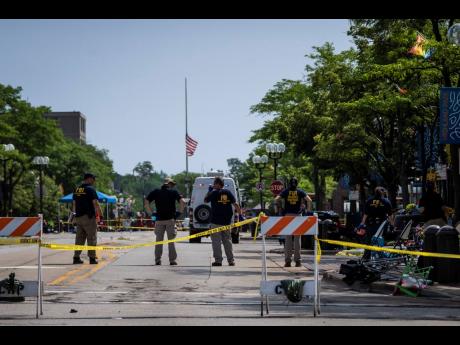 A flag hangs at half-staff as members of the FBI’s Evidence Response Team Unit investigate in downtown Highland Park, Illinois, the day after a deadly mass shooting on Monday, July 4.