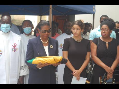 Doreen Tulloch, widow of former Tourism Minister Francis Tulloch, looks at the Jamaican flag presented to her by the police following the official funeral for the retired politician at the Blessed Sacrament Cathedral in Montego Bay, St James, on Thursday. 