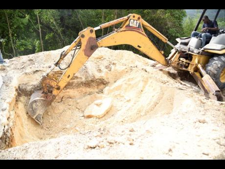 An excavator operator removes marl from the grave site in the Sutton Memorial Cemetery in Clarendon, where five members of a Clarendon family, who were killed last month, will be laid to rest.