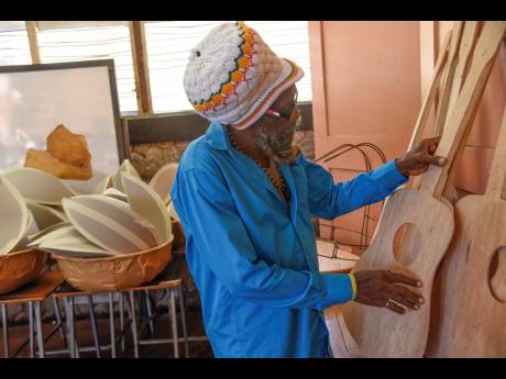 Alston Hemmings, a technical assistant, checks the smoothness of the guitar carving during the construction of costumes and accessories at a workshop set up at the Kingston Technical High School. Behind him, on the desks, are containers that will be transf