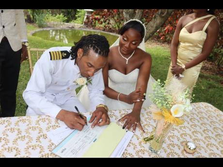 Dressed in uniform, the groom signs the papers while his beautiful bride shows her support, looking on in approval.