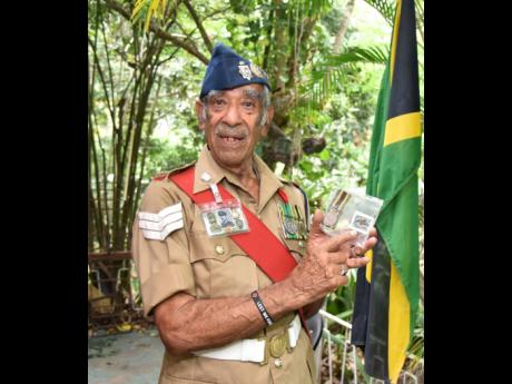Retired Sergeant Peter Williams, who raised the Jamaican flag during the ceremony to mark the island’s Independence at the Jamaica Defence Force headquarters in August 1962, points to the Independence medal that he was given and a stamp with a picture of