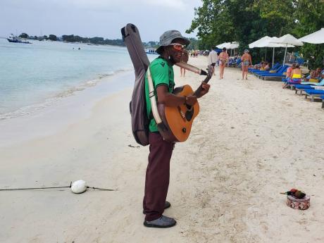 At a hotel facility next to a rundown property, a hustler began playing his guitar and singing to a group of visitors relaxing on beach chairs. None acknowledged his presence, but he continued unperturbed.