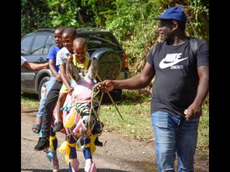 Dwayne Jones and 30-year-old donkey Pablo, dressed in leggings and colourful fabric, entertain children with a joyride at the Top Hill Donkey Racing Festival in St Catherine Monday. 