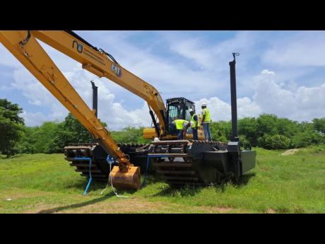 Minister of Agriculture and Fisheries Pearnel Charles Jr (right, atop vehicle) gets a quick lesson in operating the amphibious excavator at the commissioning in Rocky Hill, St Elizabeth, on Wednesday.