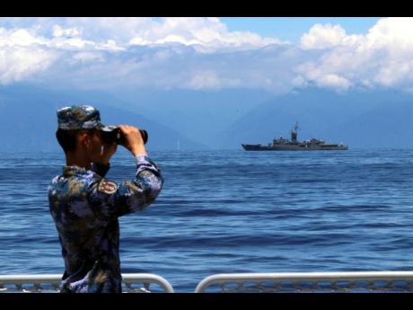 In this photo provided by China’s Xinhua News Agency, a People's Liberation Army member looks through binoculars during military exercises as Taiwan’s frigate Lan Yang is seen at the rear. 