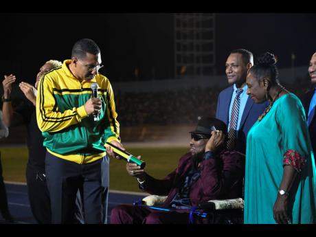 ‘Freedom March’ singer, Derrick Morgan (seated) accepts his award from Prime Minister Holness while Culture Minister, Olivia Grange, shares in the moment.