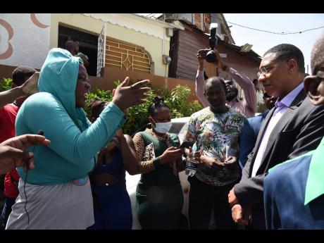 Prime Minister Andrew Holness (right) listens as a resident of central Kingston vents frustration about violent crime plaguing her community. 