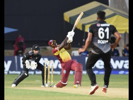 West Indies batsman Rovman Powell (centre) swings for the fences during the first T20 International of a three-match series against New Zealand at Sabina Park yesterday. Looking on are wicketkeeper Devon Conway (left) and bowler Tim Sodhi.