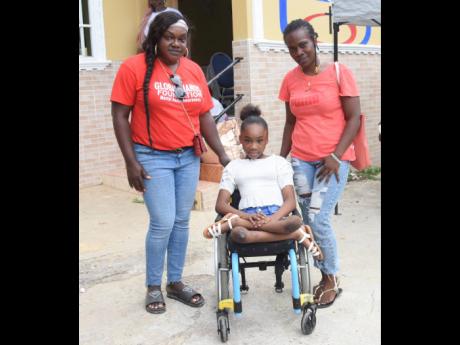 Tamara Noble (centre), who lost the ability to walk following a car accident in 2017, poses in her new wheelchair, which she received on Thursday. At right is her mom, Stacy-Ann Reeves-Noble, and Carlene Coates-Russell, the founder of the Global Hands Foun