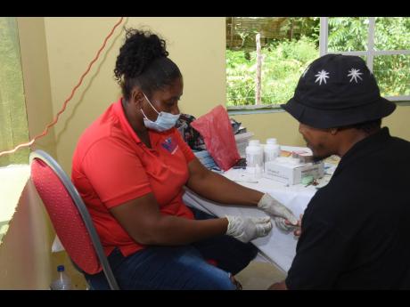 Nadine Pearce (left), medical worker with the Trelawny Health Services, takes a blood sample from Mario Duncan during the Global Hands Foundation’s Mental Health Seminar and Health Fair.