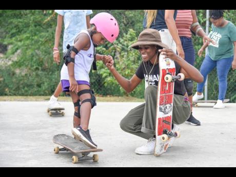 Jamaican skateboarder Kayla Wheeler assists Kharliegh Gayle with perfecting her balance and posture at the skating park in Eight Miles, Bull Bay, on Saturday. The event was aimed at inspiring self-confidence in girls.