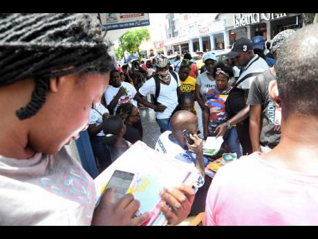 Donnaree Gooden (foreground) checks her child’s book list as others swarm Michael Smart (centre), owner of Jus Books, as he assists in the sale of back-to-school supplies from the roadside on King Street in downtown Kingston on Monday.