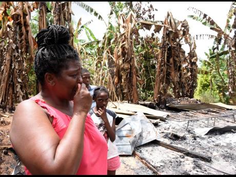 Yvonne Thompson, her son Kamoy McDonald, and daughter Amelia McDonald, of Ragsville in Guy’s Hill, St Catherine, look at the ashes of what was once their home. The house was built by Food For The Poor in February and burnt to the ground in August.  
