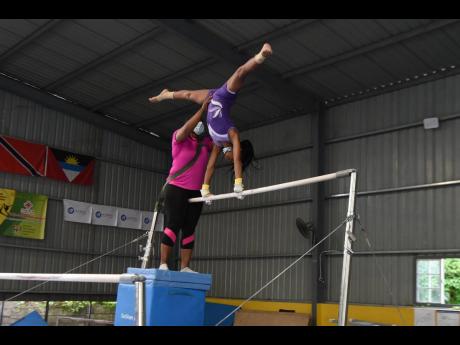 President of the Jamaica Gymnastics Association Nicole Grant-Brown assists Orchid Hall to do a handstand on the uneven bars during a practice section at the Jamaica School of Gymnastics.