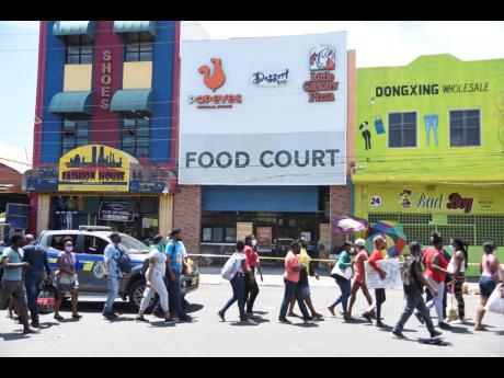 In this September 2021 photo, people walk past a scene of crime in downtown Kingston where a vendor was shot.