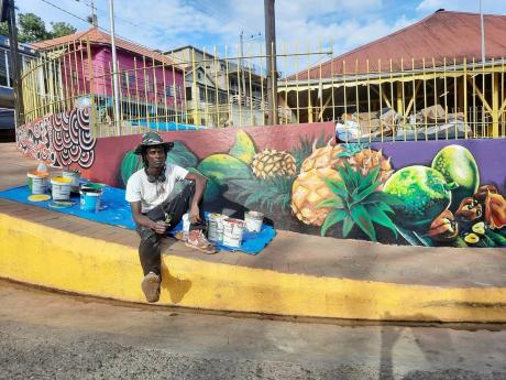 Artist Sekani Daniel sits on the sidewalk, with his work highlighted in the background. 