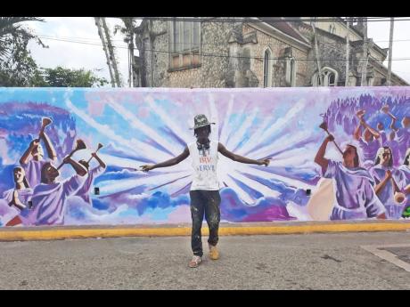 Artist Sekani Daniel, with a mural depicting trumpeters in the background.  