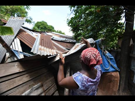 Dezreen Miller shows damage done to her home when an ackee tree fell through the roof of the structure. Pieces of old plywood, sheets of zinc and tarpaulin are used to keep out the elements.