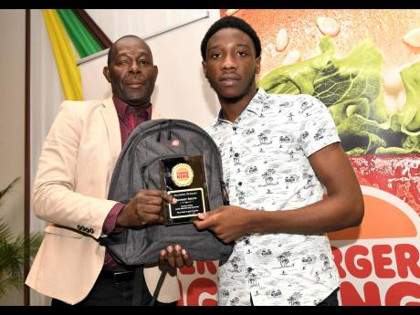 Donovan Witter (left), head of operations at Restaurant Associates Limited, presents a Burger King academic bursary to Tivoli Gardens High School student Zachary Skeine, who was one of four pupils who intervene to break up a physical clash between a studen