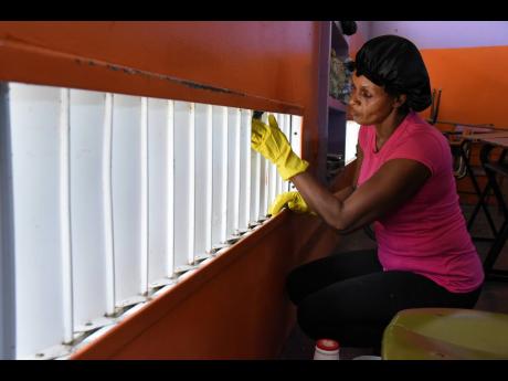 Marcia Hayles cleans windows in a classroom at Friendship Primary in Spanish Town. The school is not far from the crime hotspot of St John’s Road, the site of ongoing gang violence this year.