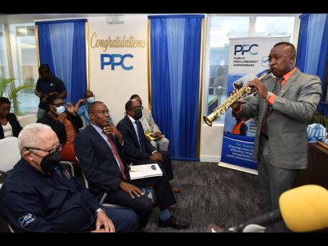 Finance and the Public Service Minister Dr Nigel Clarke (centre) is entranced by saxophonist Leeroy Newell (right) during the Public Procurement Commission (PPC) Milestone Presentation Ceremony held at the PanJam building in New Kingston on Wednesday. Clar