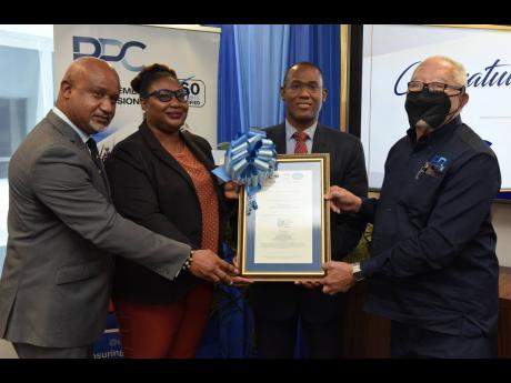 Navenia Wellington-Ford (second left), manager, National Certification Body of Jamaica, presents the ISO 9001:2015 certificate to Finance and the Public Service Minister Dr Nigel Clarke (second right); Lt Com (Ret’d) Paul Wright (left), executive directo