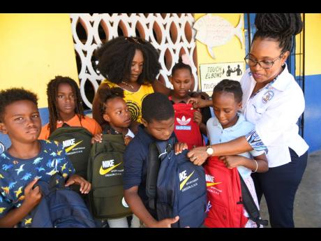 Nickeisha Walsh (right), executive director of Students’ Loan Bureau (SLB), and Port Royal Primary and Infant School Principal Nicola Jones present school bags to students on Friday. The SLB also donated appliances to the school, which is the first under