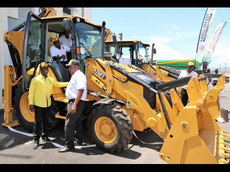 Acting Chief Executive Officer of the Rural Agricultural Development Authority (RADA), Winston Simpson ( left, foreground), with Minister of State in the Ministry of Agriculture and Fisheries, Frank Witter, at the handing over of CAT 426F2 backhoes last We