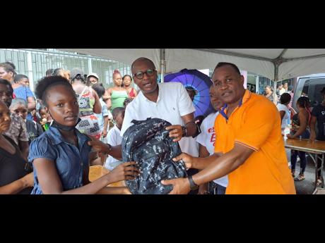 Britannia Douglas, a grade seven student at Little London High School accepts a school bag from Ian Hayles, People’s National Party chairman for the Westmoreland western constituency, Shirlet Craig-Davis, principal of Little London Primary School, partia